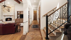 Un vaste espace de vie agrémenté d’une cheminée, d’un canapé en cuir rouge et d’un parquet en bois disposé en chevrons.