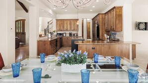 Une cuisine spacieuse avec des meubles en bois, un îlot central et un coin repas agrémenté de verrerie bleue et d’une plante en pot.