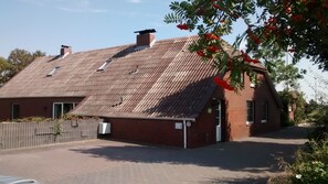 Traditional brick building with a sloped roof and chimney, set amidst a paved area with a wooden fence.