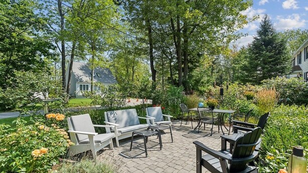 An outdoor patio with seating and tables, surrounded by lush greenery and flowering plants.
