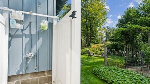 A white exterior wall with a utility box, a small garden area with a wooden fence, and a grassy lawn.