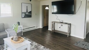 Ein Wohnzimmer mit flachbildfernseher an der Wand, einem grauen Sofa, einem weißen Couchtisch mit einer dekorativen Vase und einem Holzkonsolentisch.