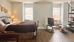 A bedroom with a bed, bedside table, lamp, TV, and a small desk. - Downtown studio apartment with ROOFTOP DECK (Bloomington)