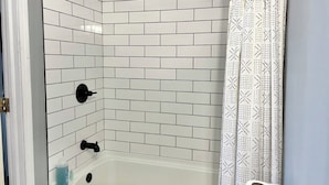 A bathroom with white subway tiles, a black showerhead, and a patterned shower curtain. - Downtown studio apartment with ROOFTOP DECK (Bloomington)
