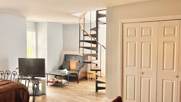 A modern living room with a TV, sofa, and staircase. - Downtown studio apartment with ROOFTOP DECK (Bloomington)