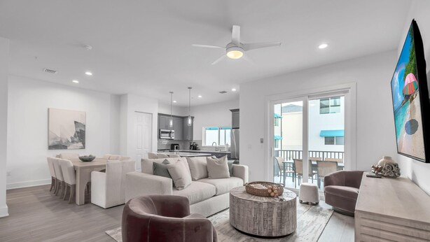 Ein modernes Wohnzimmer mit Sofa, Sesseln und Couchtisch. Ein Essbereich mit Tisch und Stühlen sowie eine Küche im Hintergrund sind ebenfalls zu sehen.