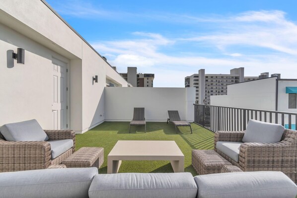 Une terrasse sur le toit, aménagée avec des meubles en osier, une table et un petit espace gazonné.
