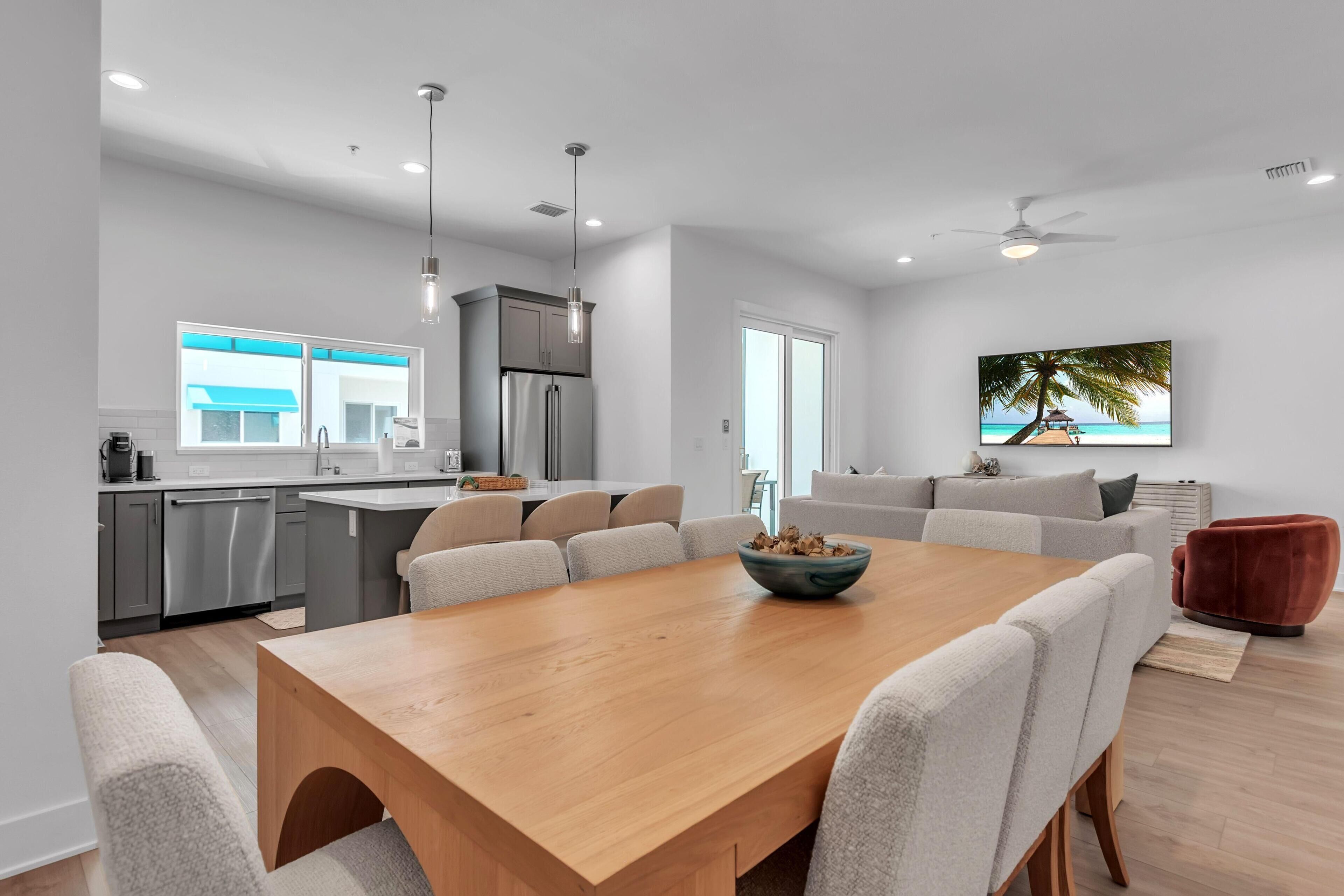 A modern kitchen with a dining area, a large window, and a ceiling fan.