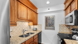 Una cocina con gabinetes de madera, encimeras de granito, electrodomésticos de acero inoxidable y salpicadero de azulejos.