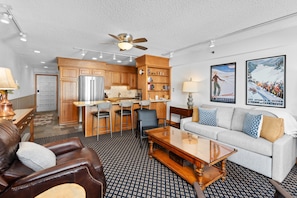 Une chambre d’hôtel moderne dotée d’une kitchenette, d’un coin repas, d’un salon avec un canapé et un fauteuil, et d’un ventilateur de plafond.