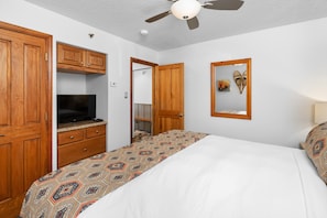 Une chambre à coucher comprenant un lit, une armoire en bois, une télévision, un ventilateur de plafond et un miroir.