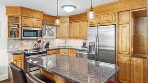 A modern kitchen with granite countertops, stainless steel appliances, wooden cabinets, and a central island with bar stools.