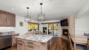 A modern kitchen with wooden cabinets, granite countertops, and a central island. There is a dining area with a wooden table and chairs, and a fireplace. - Crestwood 1201 Premier 3 Bedroom (Snowmass Village)