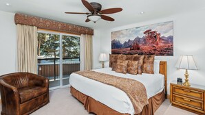 A bedroom with a large bed, a ceiling fan, a sofa, a nightstand, and a painting of a mountain landscape. - Crestwood 1202 Deluxe 3 Bedroom (Snowmass Village)