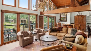 A spacious living room with large windows, a chandelier, and a cozy seating area.