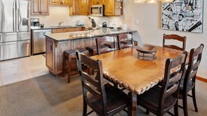 A kitchen with wooden cabinets, stainless steel appliances, and a central island with chairs. - Crestwood 1207 Deluxe 3 Bedroom plus Loft (Snowmass Village)