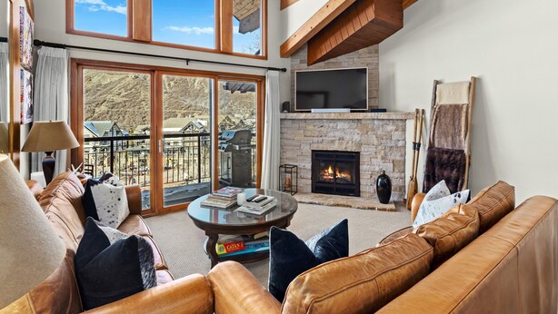 A spacious living room with leather sofas, a fireplace, and large windows offering a view of the outdoors. - Crestwood 1207 Deluxe 3 Bedroom plus Loft (Snowmass Village)