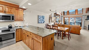A kitchen with wooden cabinets, a large island, and a dining area with a view of mountains. - Crestwood 1207 Deluxe 3 Bedroom plus Loft (Snowmass Village)