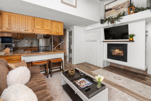 A modern living room with a fireplace, wooden cabinets, and a kitchen area.