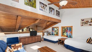 A spacious room with a high ceiling, wooden beams, a large bed, a sofa, a TV, and a window with colorful curtains. - Crestwood 1212 Standard 2 Bedroom plus Loft (Snowmass Village)