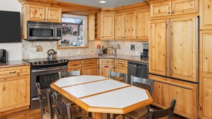 A kitchen with wooden cabinets, a stainless steel refrigerator, a microwave, an oven, and a dining table with chairs. - Crestwood 1212 Standard 2 Bedroom plus Loft (Snowmass Village)