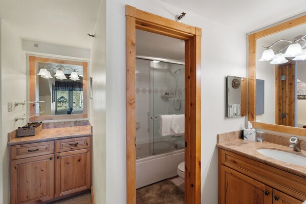 A bathroom with wooden cabinets, a sink, a mirror, and a glass-enclosed shower.