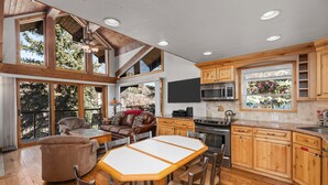 A spacious kitchen with wooden cabinets, a dining table with chairs, and a large window overlooking a forested area. - Crestwood 1212 Standard 2 Bedroom plus Loft (Snowmass Village)