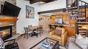 A spacious living area with a fireplace, a dining table with chairs, a sofa, a coffee table, and a bookshelf.