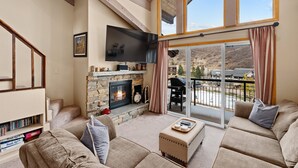 Una sala de estar acogedora con chimenea, asientos confortables, un televisor de pantalla plana y un balcón con vistas panorámicas.
