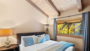 Una cama bien hecha con un edredón a rayas, una lámpara de noche y una ventana con cortinas.