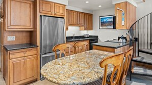 Una cocina con armarios de madera, un refrigerador de acero inoxidable, una encimera de granito y un comedor con mesa y sillas.