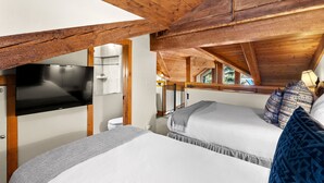 Un dormitorio con dos camas, una televisión de pantalla plana, vigas de madera y vistas al exterior.
