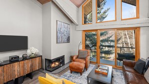 A modern living room with a fireplace, leather furniture, and large windows offering a view of the outdoors.