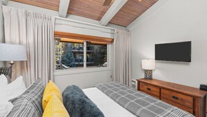 A bedroom with a bed, a nightstand, a lamp, a TV, and a window with curtains.