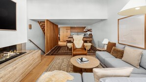 Un salon moderne avec une cheminée, un canapé et une table basse. Un escalier mène à un espace cuisine.