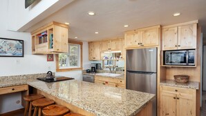 Une cuisine moderne avec des meubles en bois, des plans de travail en granit, des appareils électroménagers en acier inoxydable et des tabourets en bois.