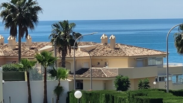 A coastal building with a tiled roof, surrounded by palm trees and a clear view of the sea. - Spacious Apartment With all Facilities Just a few Metres From the Beach (Benalmádena)