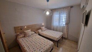 A bedroom with two beds, a ceiling light, a window with curtains, and a wall-mounted TV. - Spacious Apartment With all Facilities Just a few Metres From the Beach (Benalmádena)