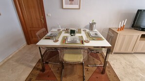 A dining area with a table set for four, clear chairs, a television, and a framed picture on the wall. - Spacious Apartment With all Facilities Just a few Metres From the Beach (Benalmádena)