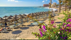 A beach with rows of sun loungers and umbrellas, a sandy shore, and a building in the background. - Spacious Apartment With all Facilities Just a few Metres From the Beach (Benalmádena)