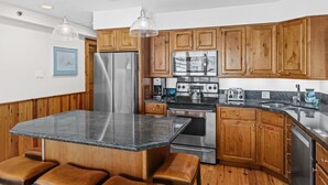 A kitchen with wooden cabinets, a stainless steel refrigerator, a gas stove, and a granite countertop.