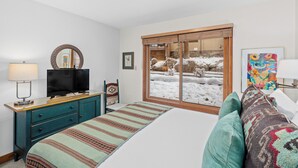 A bedroom with a bed, a TV on a dresser, a window with a view of snow outside, and a painting on the wall.