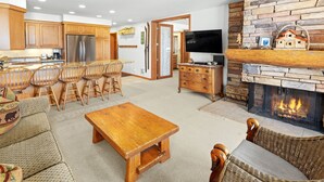 A spacious living room with a fireplace, wooden furniture, and a kitchen area with modern appliances.