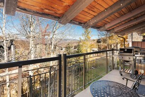 Un balcón con vistas a un paisaje montañoso, una parrilla y una mesa redonda con sillas.