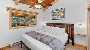 Ein Schlafzimmer mit einem Bett, einem Deckenventilator, einem Fenster mit Blick auf Bäume und einem gerahmten Bild an der Wand.