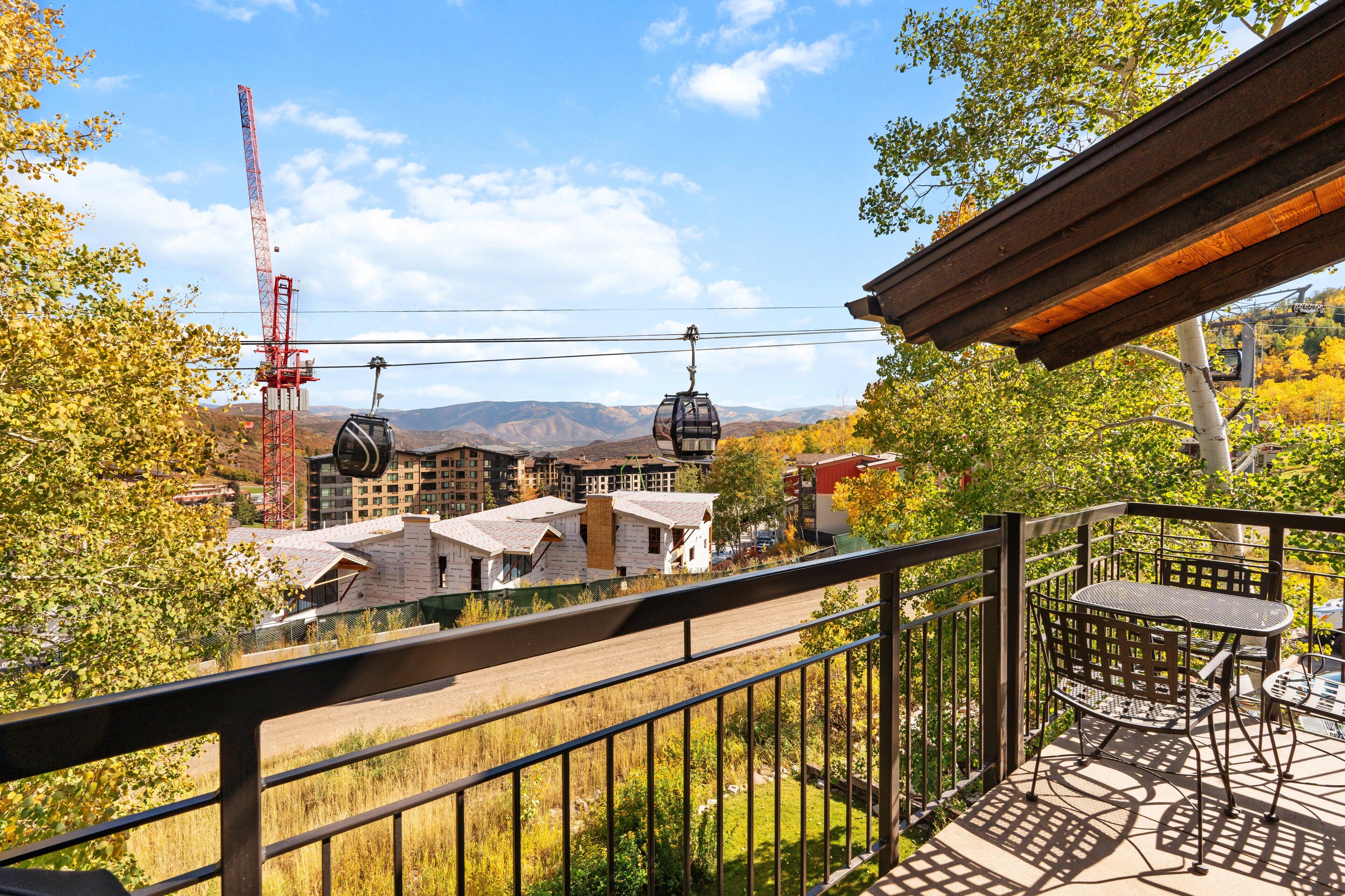 A balcony with a table and chairs, overlooking a mountainous landscape with buildings and a crane.