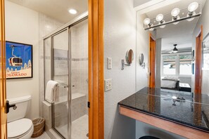 A bathroom with a glass shower enclosure, a white toilet, and a black countertop with a mirror above it.