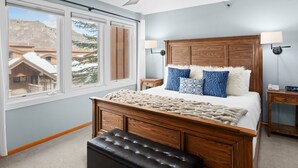 A bedroom with a large bed, wooden headboard, two bedside lamps, a ceiling fan, and a view of snow-covered buildings. - Crestwood 2108 Deluxe 2 Bedroom (Snowmass Village)