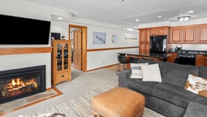 A living room with a fireplace, a gray sofa, an ottoman, and a television. - Crestwood 2108 Deluxe 2 Bedroom (Snowmass Village)