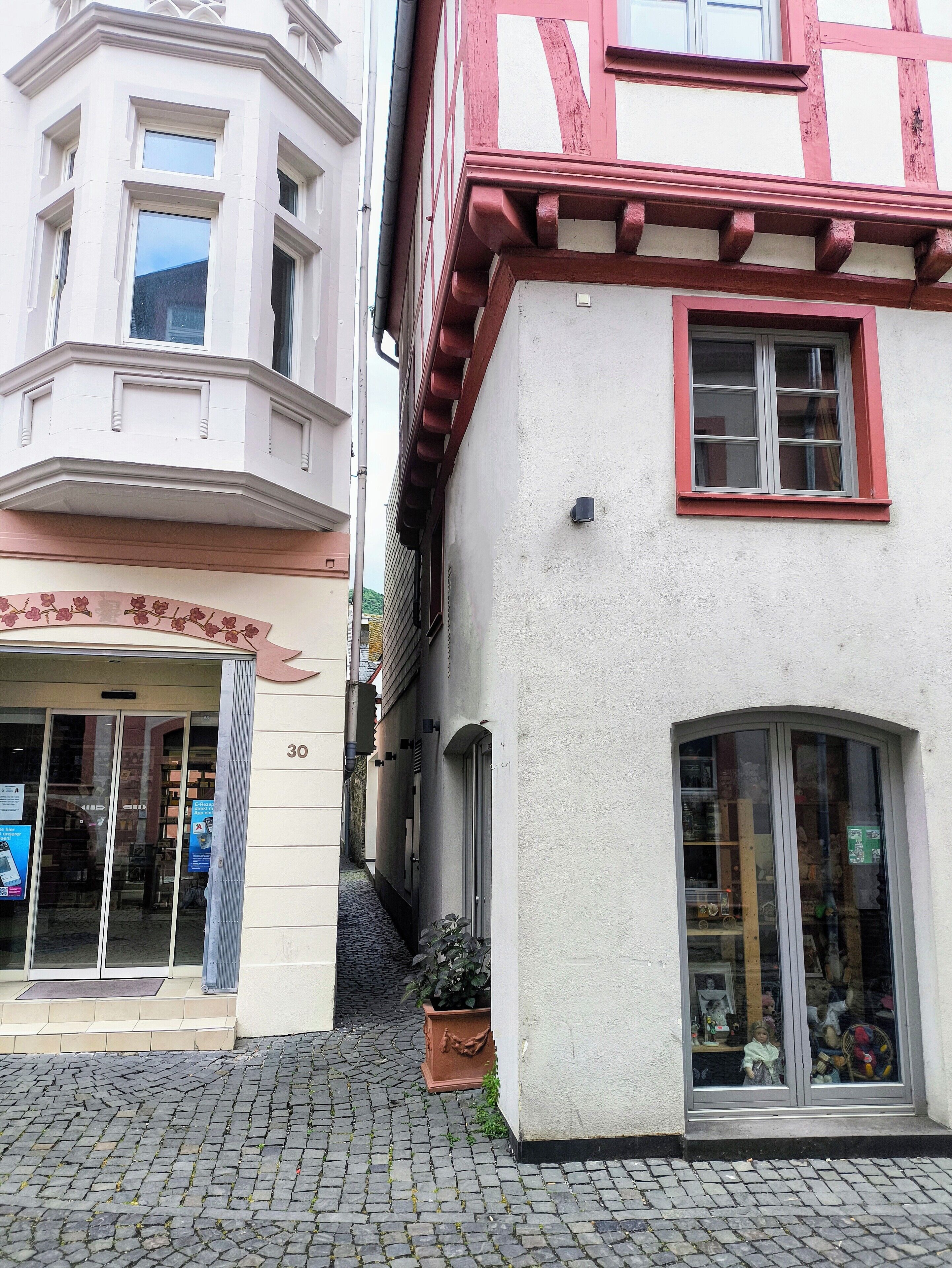 Een smalle straat met keien, met gebouwen in traditionele Europese stijl, waaronder een winkel met glazen deuren en een etalage.